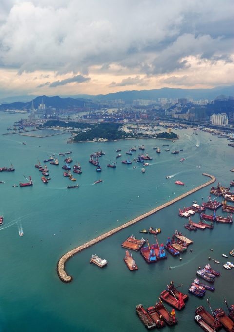 Victoria Harbor aerial view and skyline in Hong Kong with urban skyscrapers and boats.